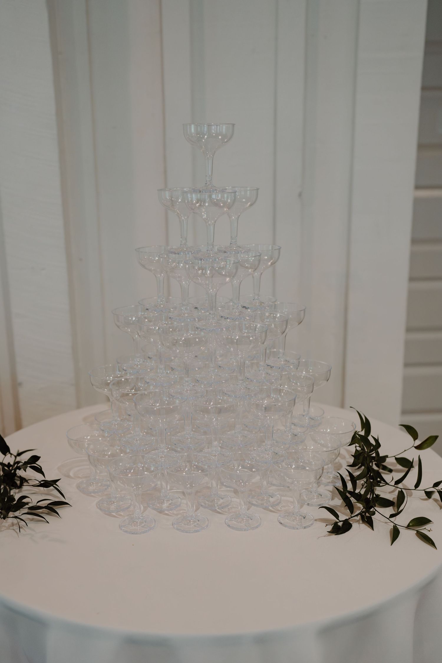 Crystal champagne glasses arranged in tiers on white reception table.