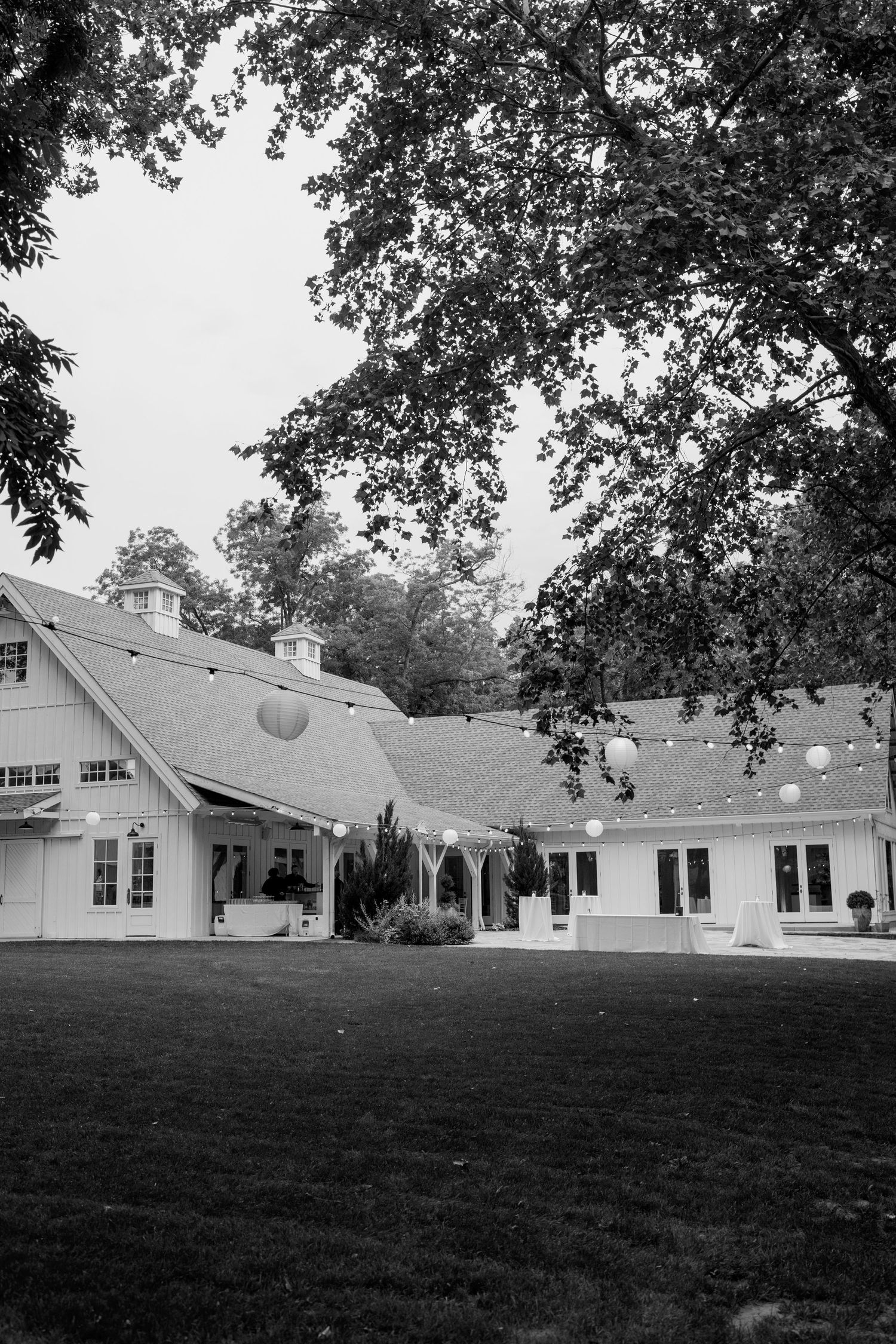 Black and white exterior view of a charming white barn-style venue with manicured lawn.