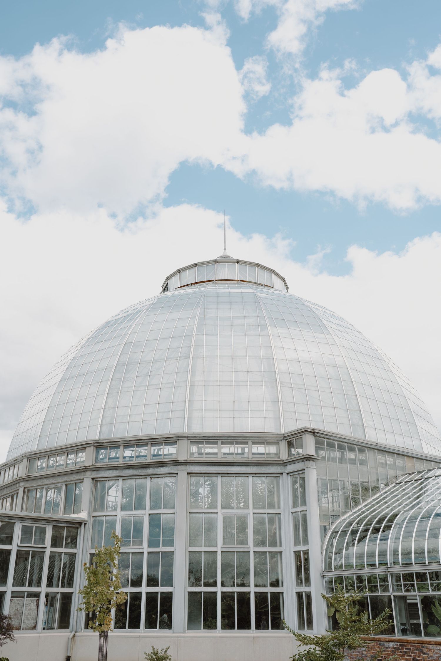 Large glass dome conservatory building with white steel frame structure against blue sky with white clouds.