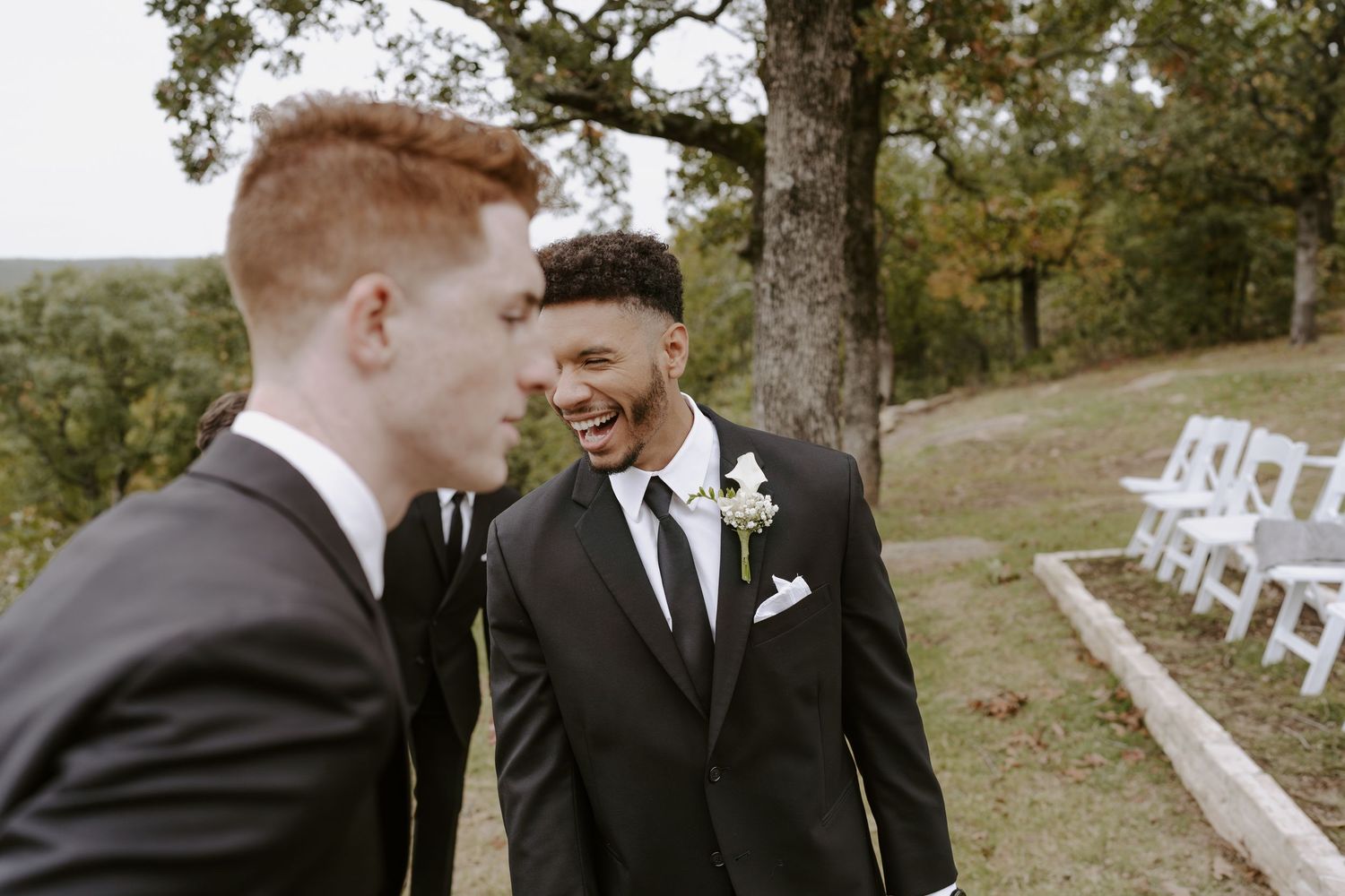 Two people share a candid moment of laughter during an outdoor wedding ceremony.