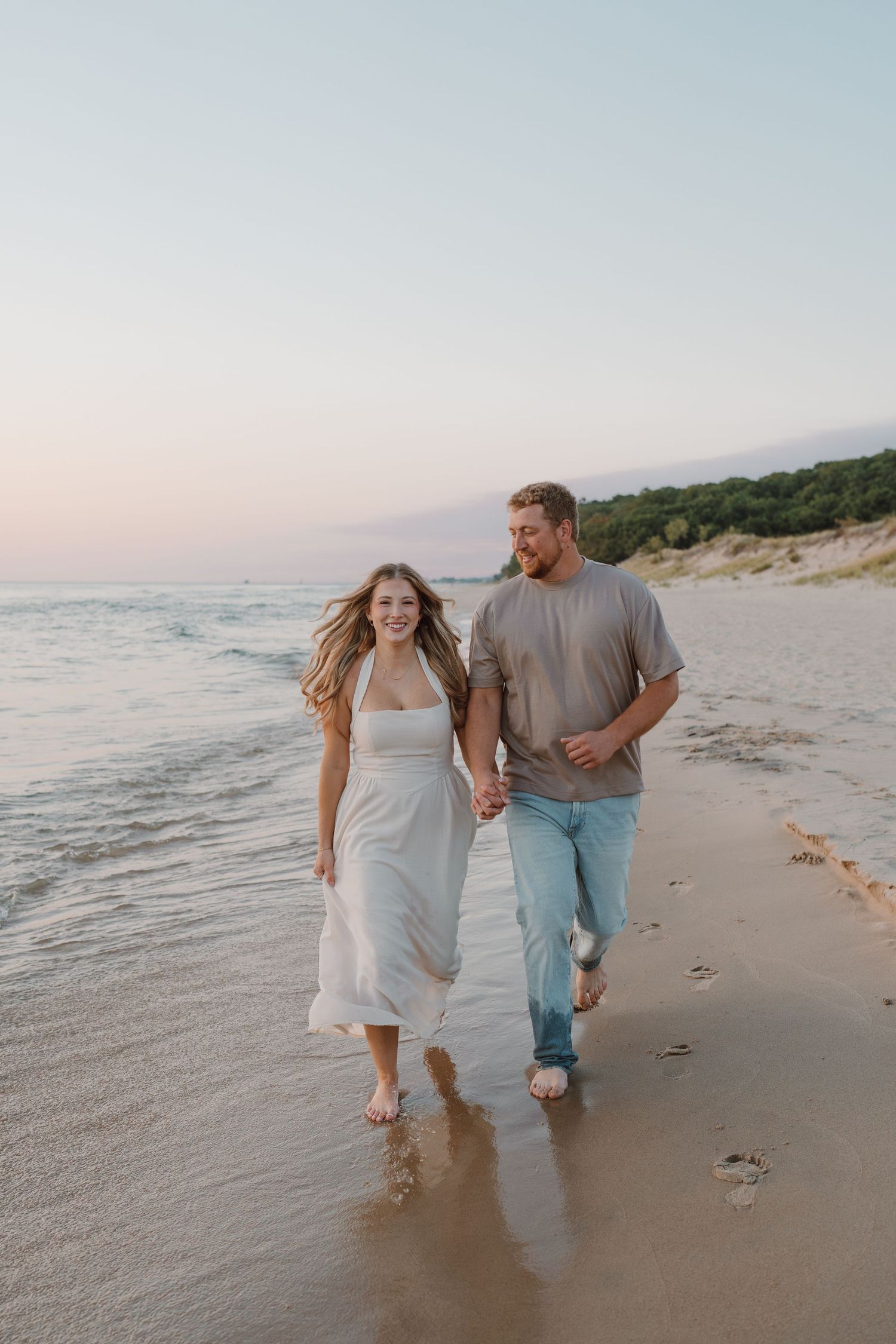 A couple walks playfully along the beach at sunset holding hands and enjoying the ocean waves.