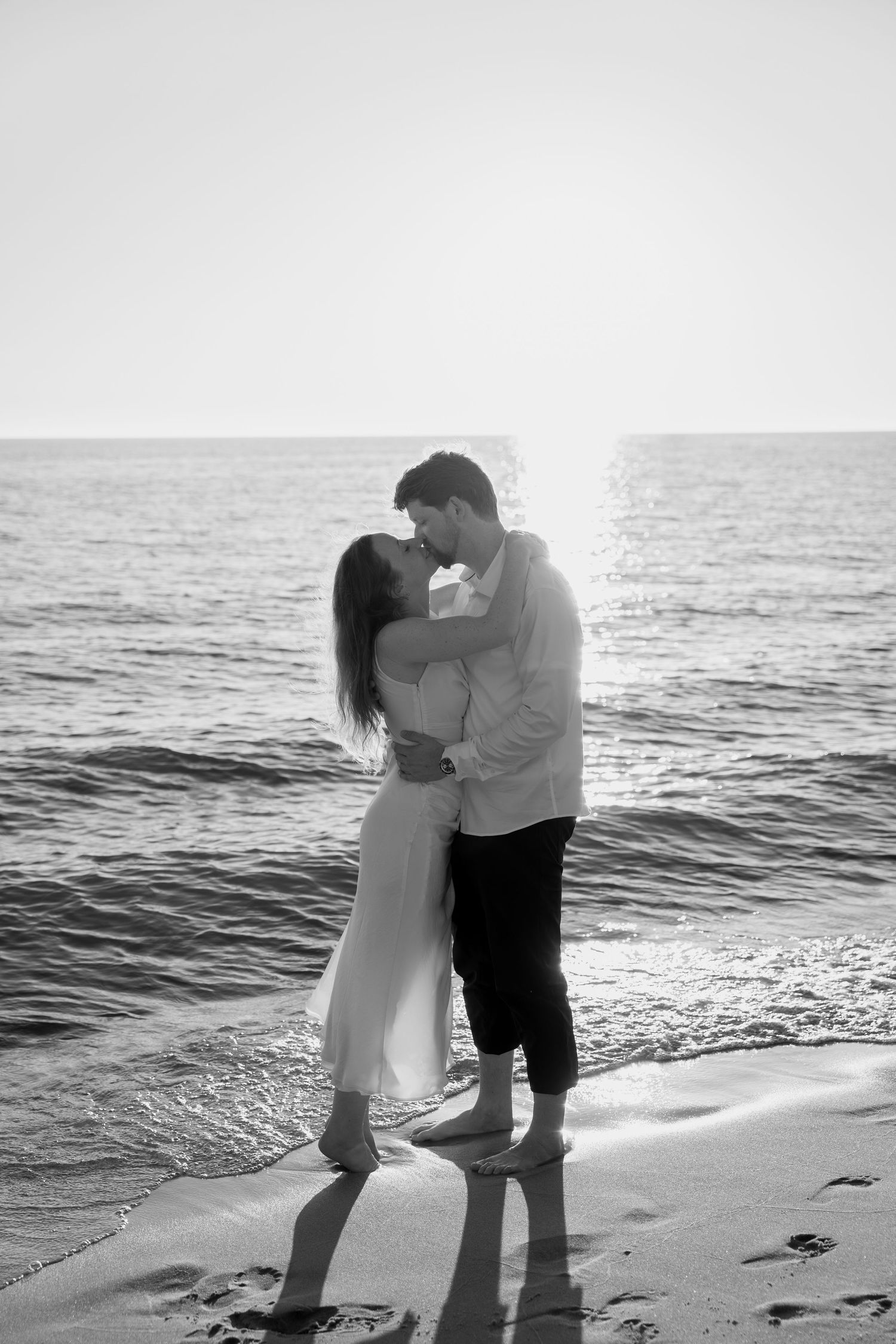 A black and white capture of a couple's romantic beach embrace at sunset.