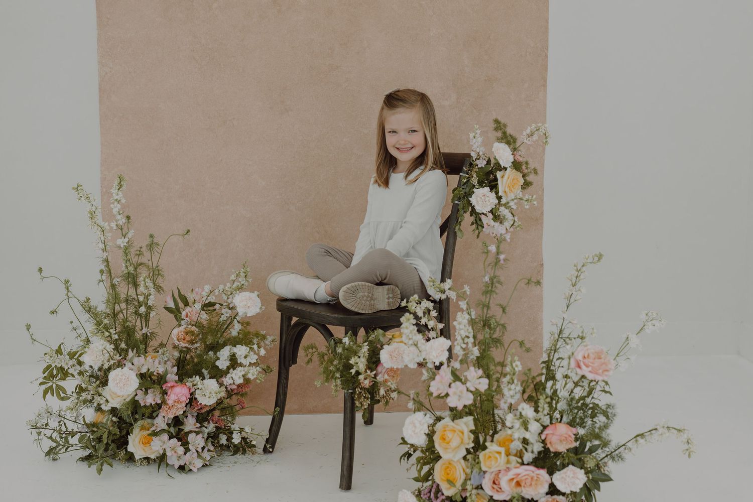 Professional photography setup featuring spring floral arrangements and rustic chair against beige backdrop.