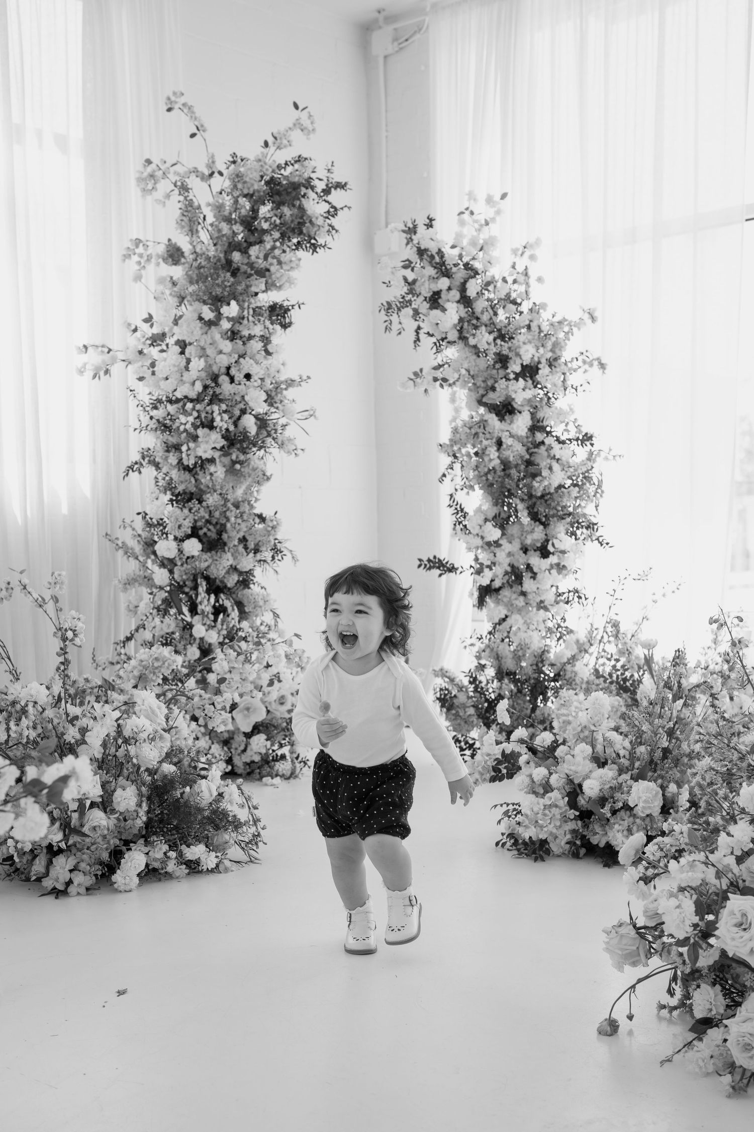 Black and white photo of a joyful moment in a studio decorated with elegant floral arrangements.