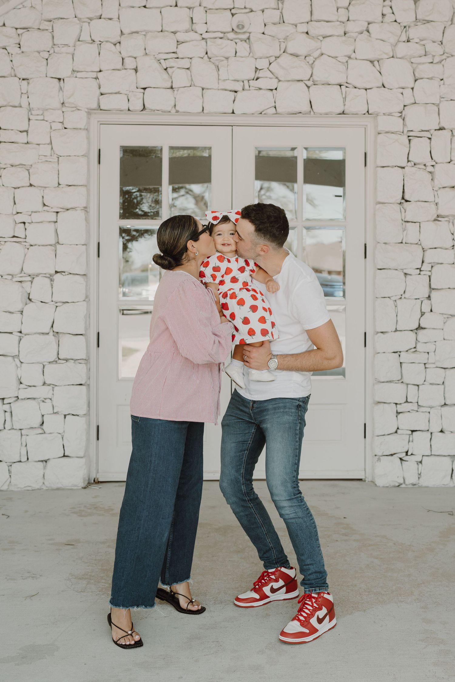 Sweet family moment captured in front of white stone wall with glass doors.