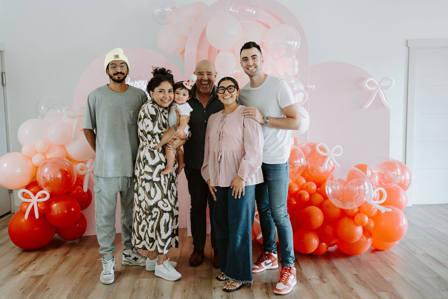 Family gathering in front of a festive balloon display with coral and pink decorations.