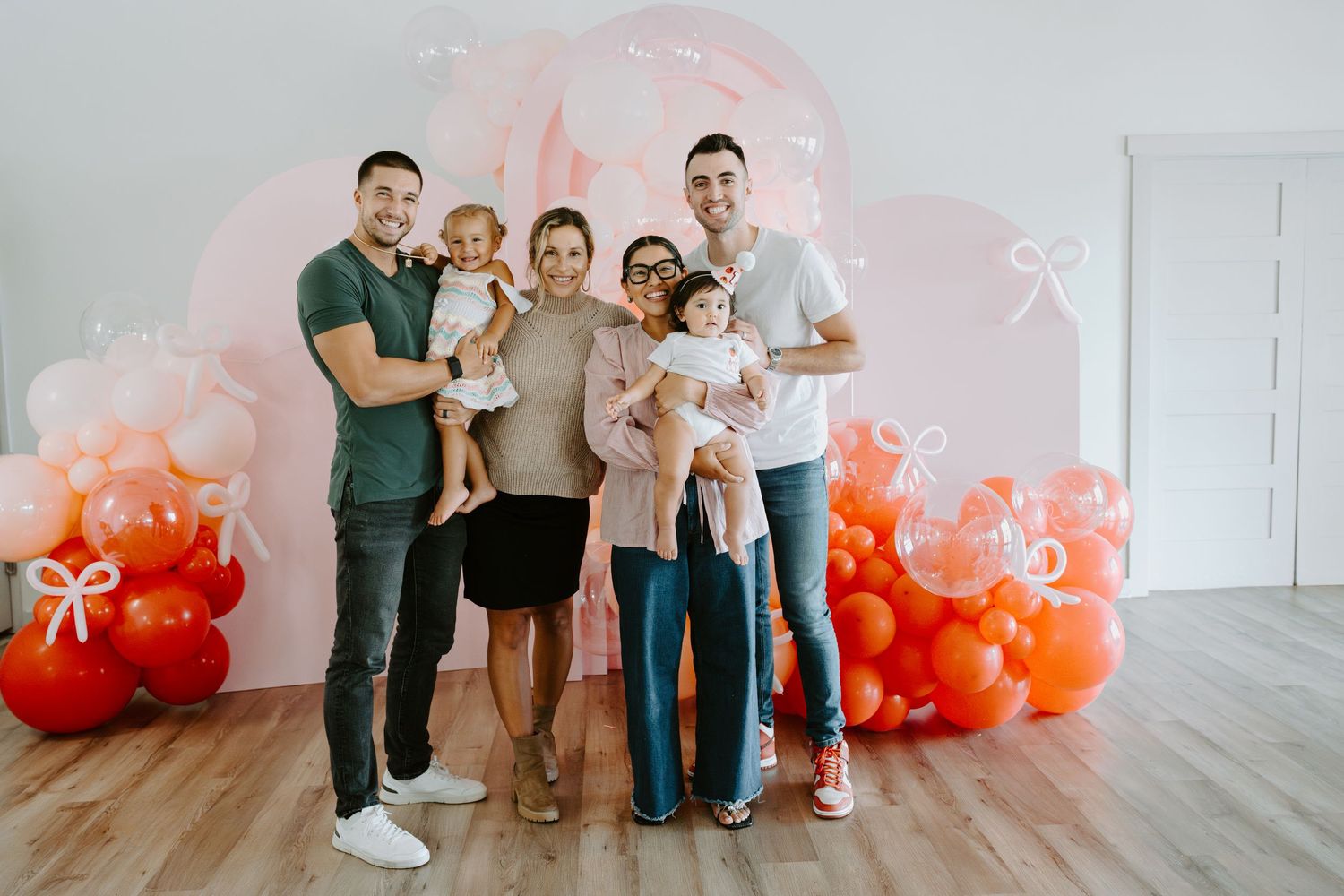 Extended family gathering in front of decorative balloon arrangement at birthday party.