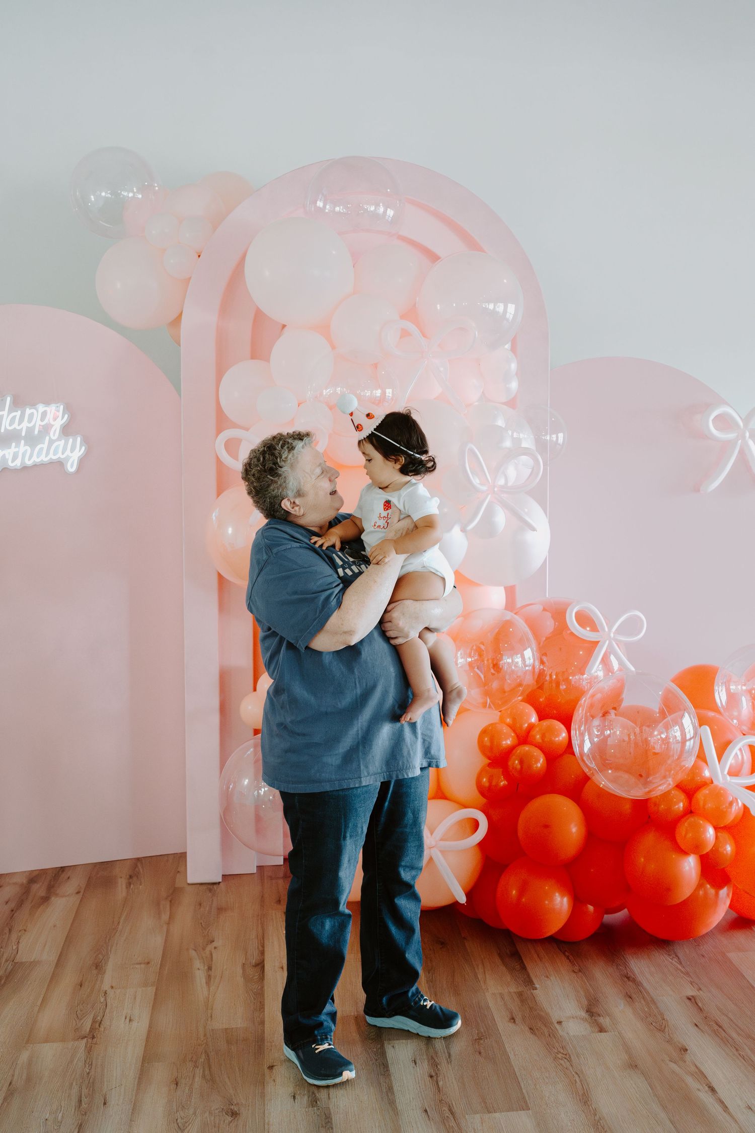 Sweet family moment captured against a backdrop of pink and orange balloons.