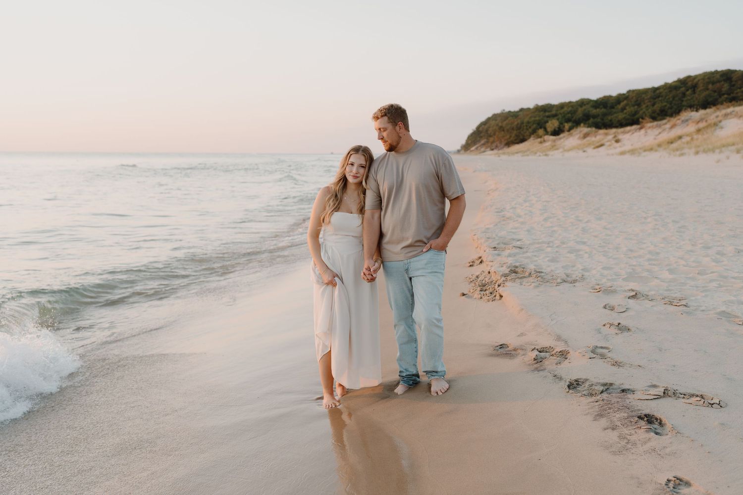 Romantic beach photoshoot at sunset with couple walking along the shoreline.