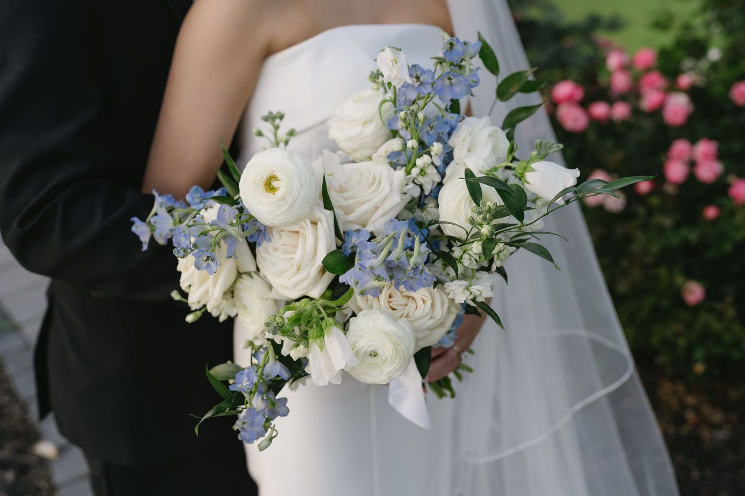 Bride holding a romantic bouquet of white roses and blue delphinium flowers on her wedding day.