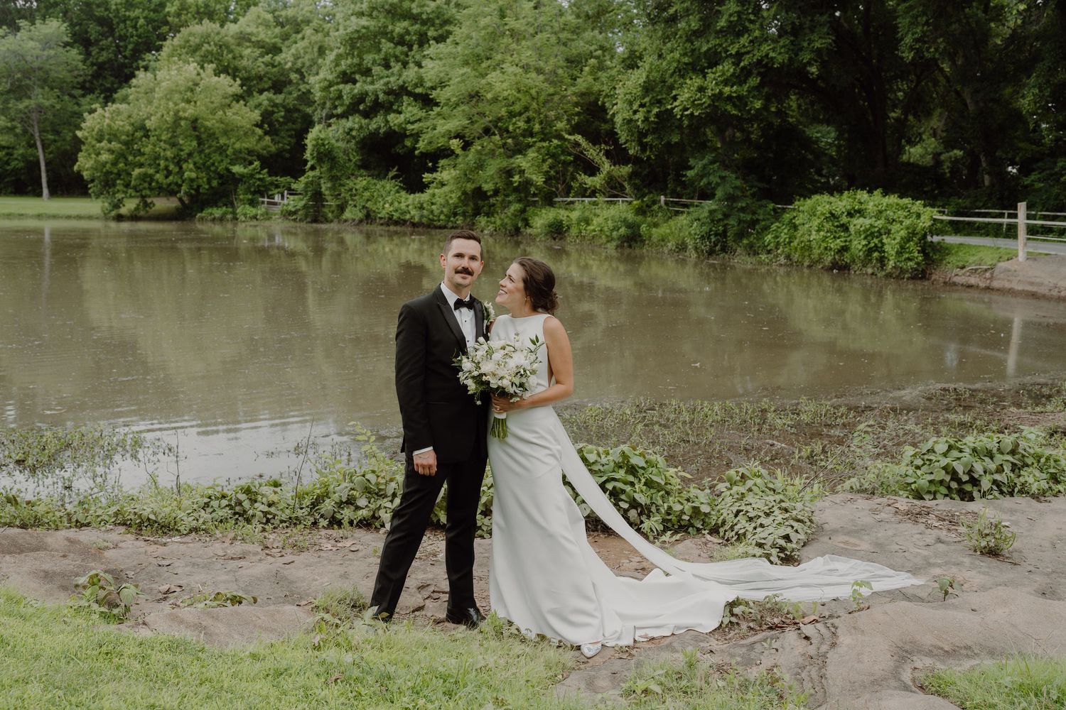 Scenic lakeside wedding photography with long white dress and natural greenery.