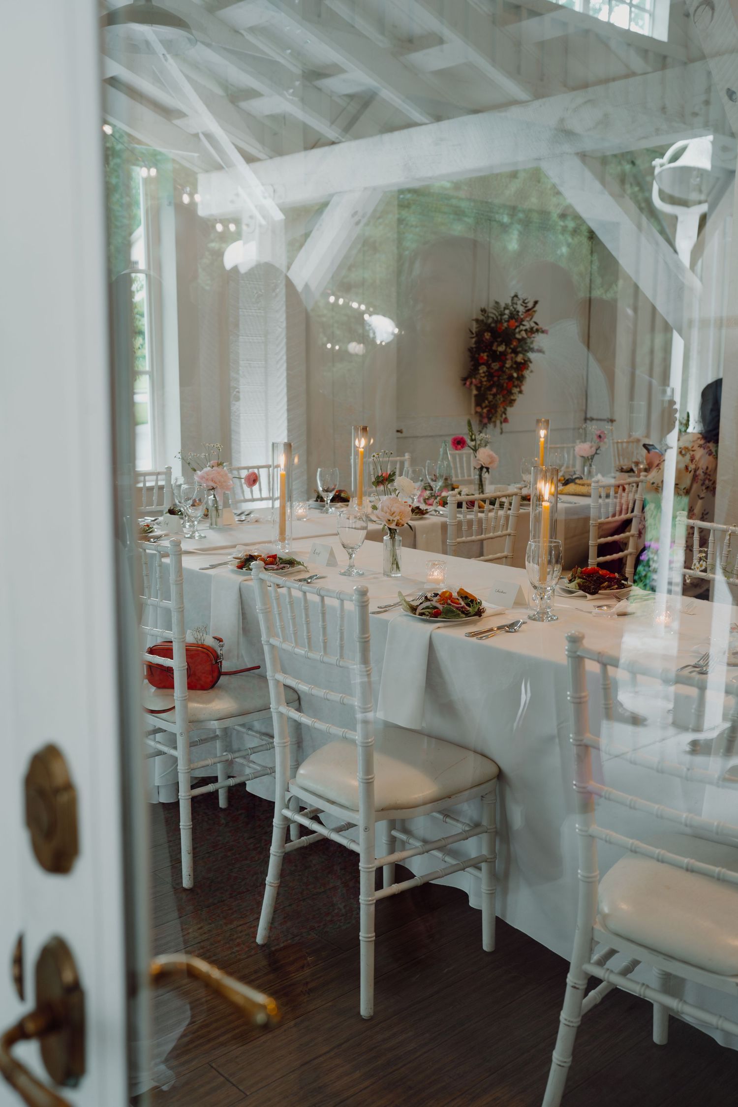Elegant white wedding reception venue with long tables set for dining under wooden beams.