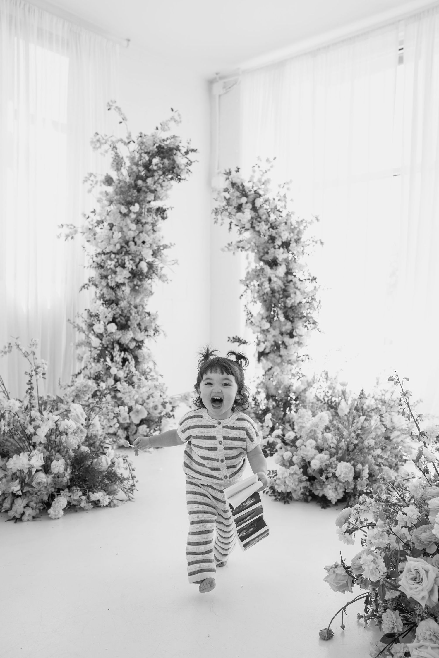 Joyful moment captured in a white studio surrounded by elegant floral arrangements.