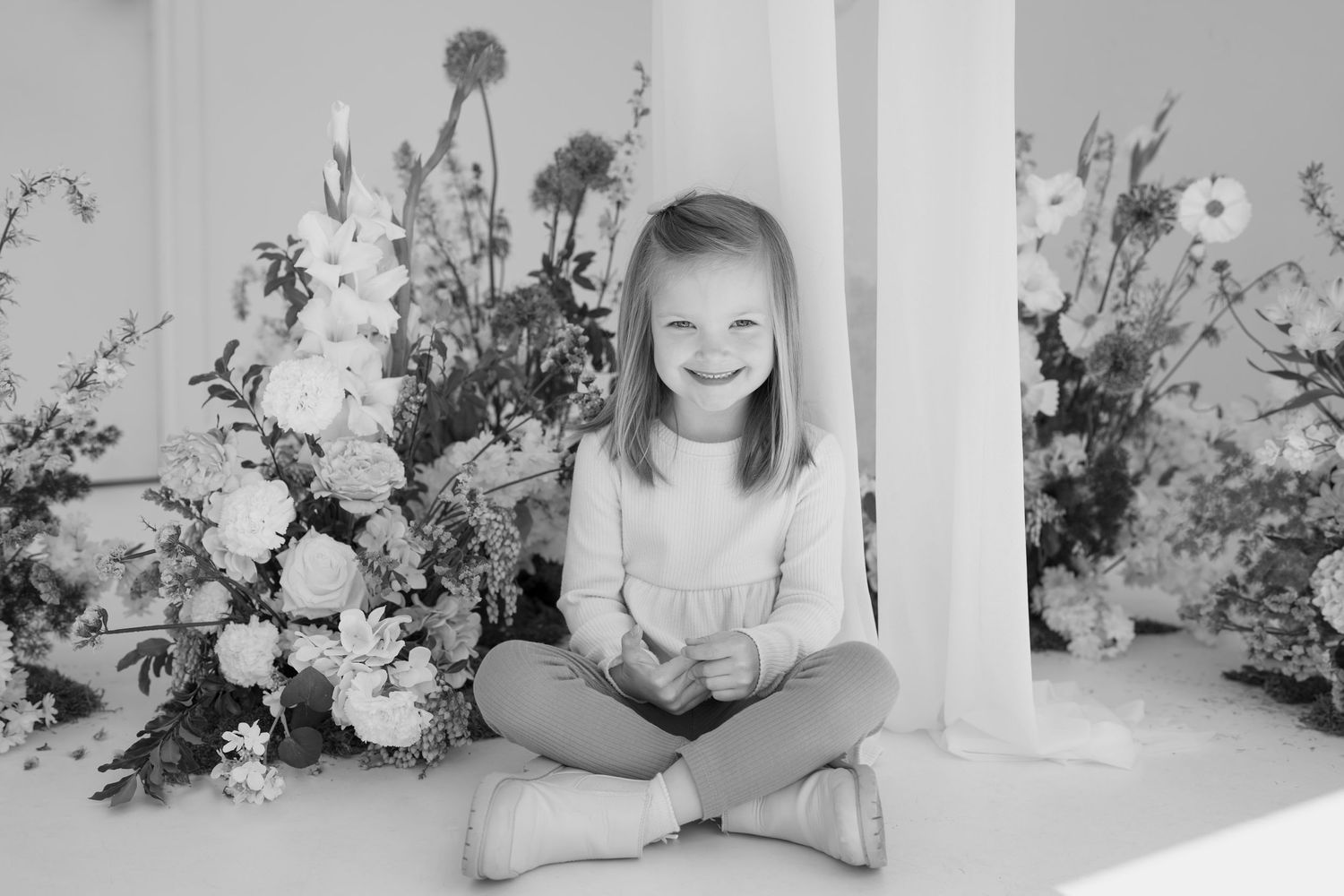 Black and white portrait surrounded by elegant floral arrangements in a bright studio setting.