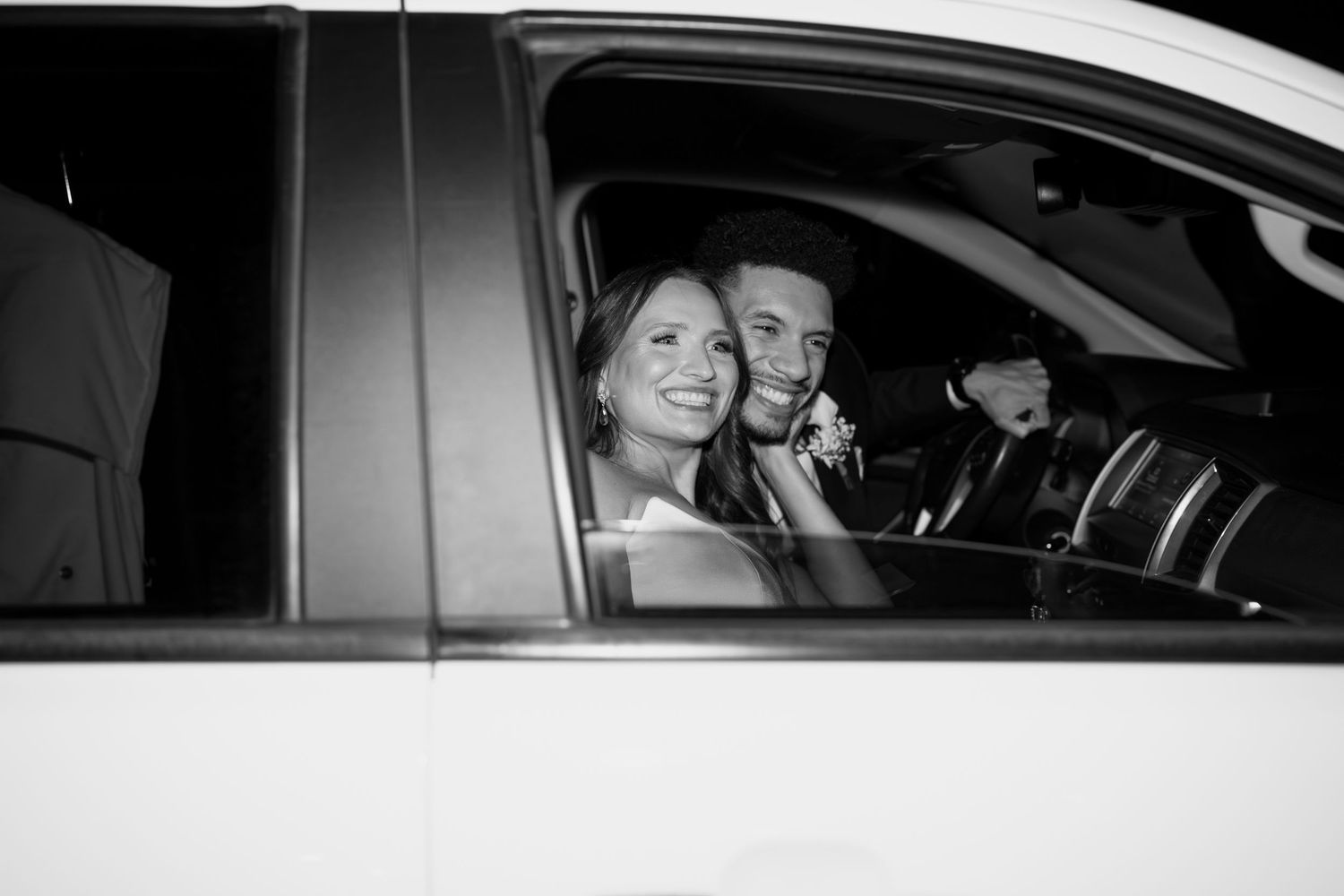Black and white photo of a couple in a car departing from their wedding celebration.