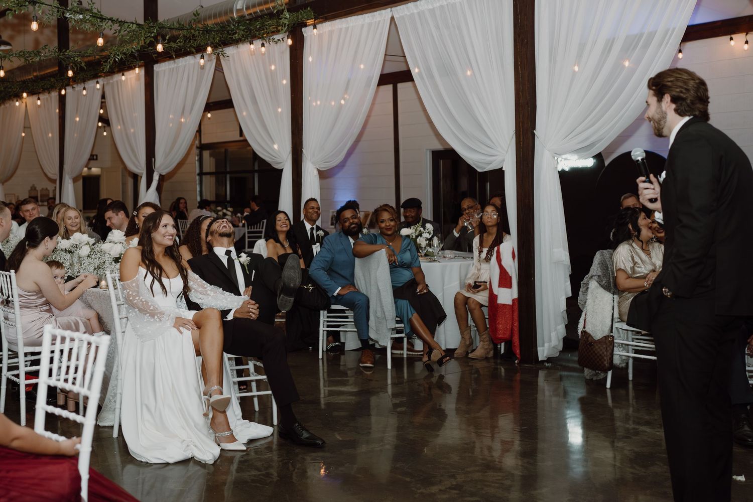 Wedding venue interior with exposed beams, string lights, and white drapery creating a romantic atmosphere.