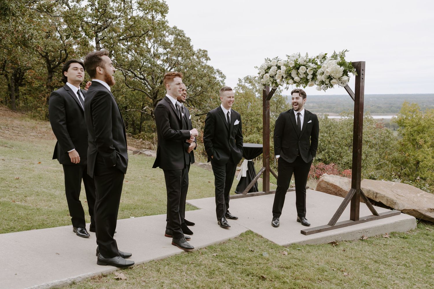 Groomsmen in formal attire gather on outdoor path with scenic mountain views.