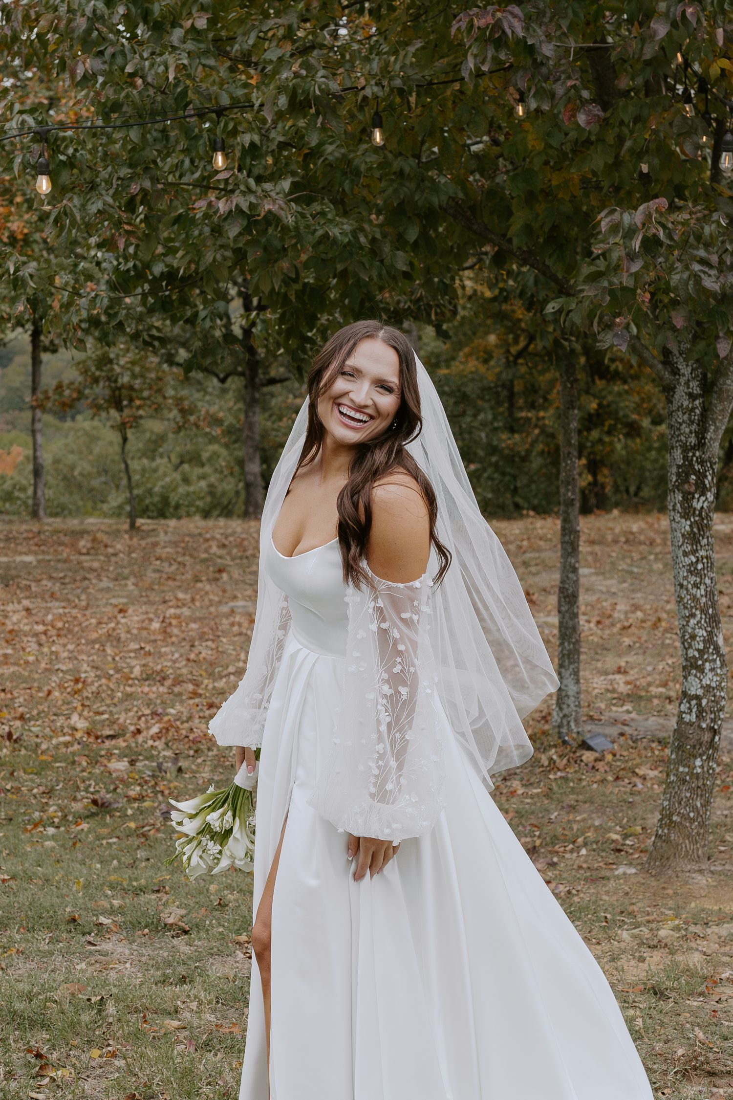A flowing white wedding dress with lace sleeves captured in an autumn outdoor setting.