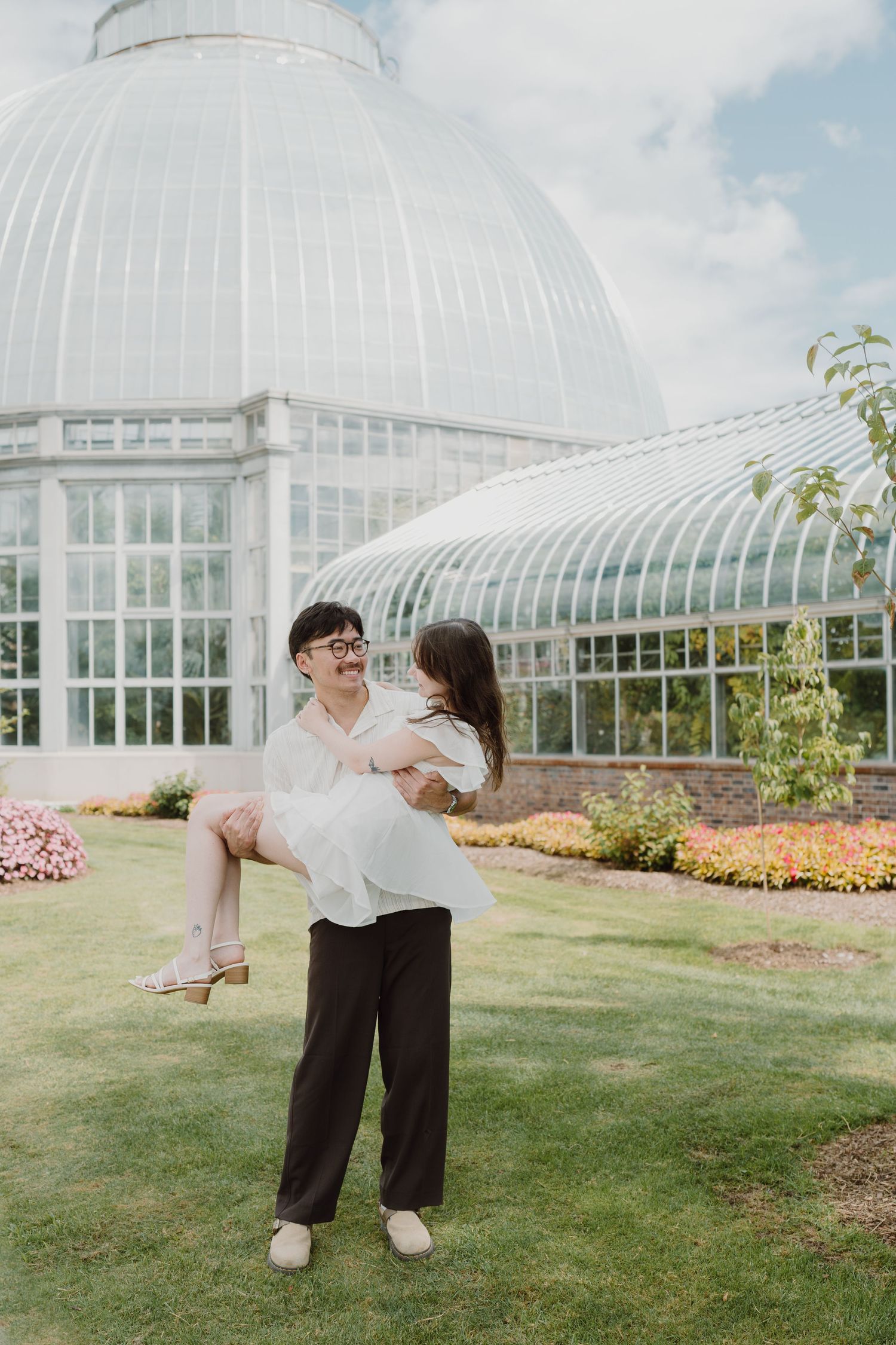 A couple dancing and embracing on grass with a white conservatory building in the background.