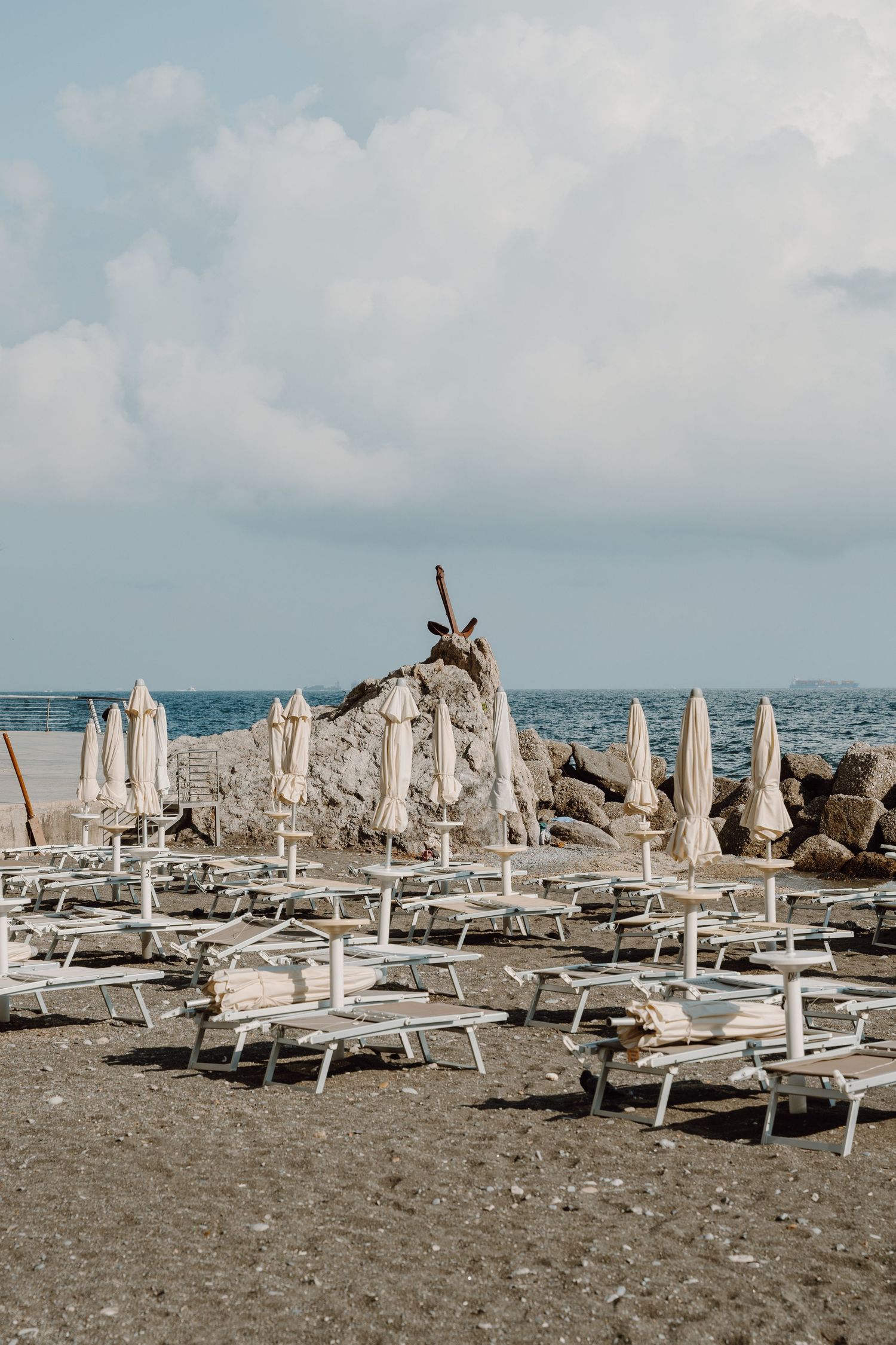Beach scene with rows of white umbrellas and lounge chairs on a rocky shoreline.