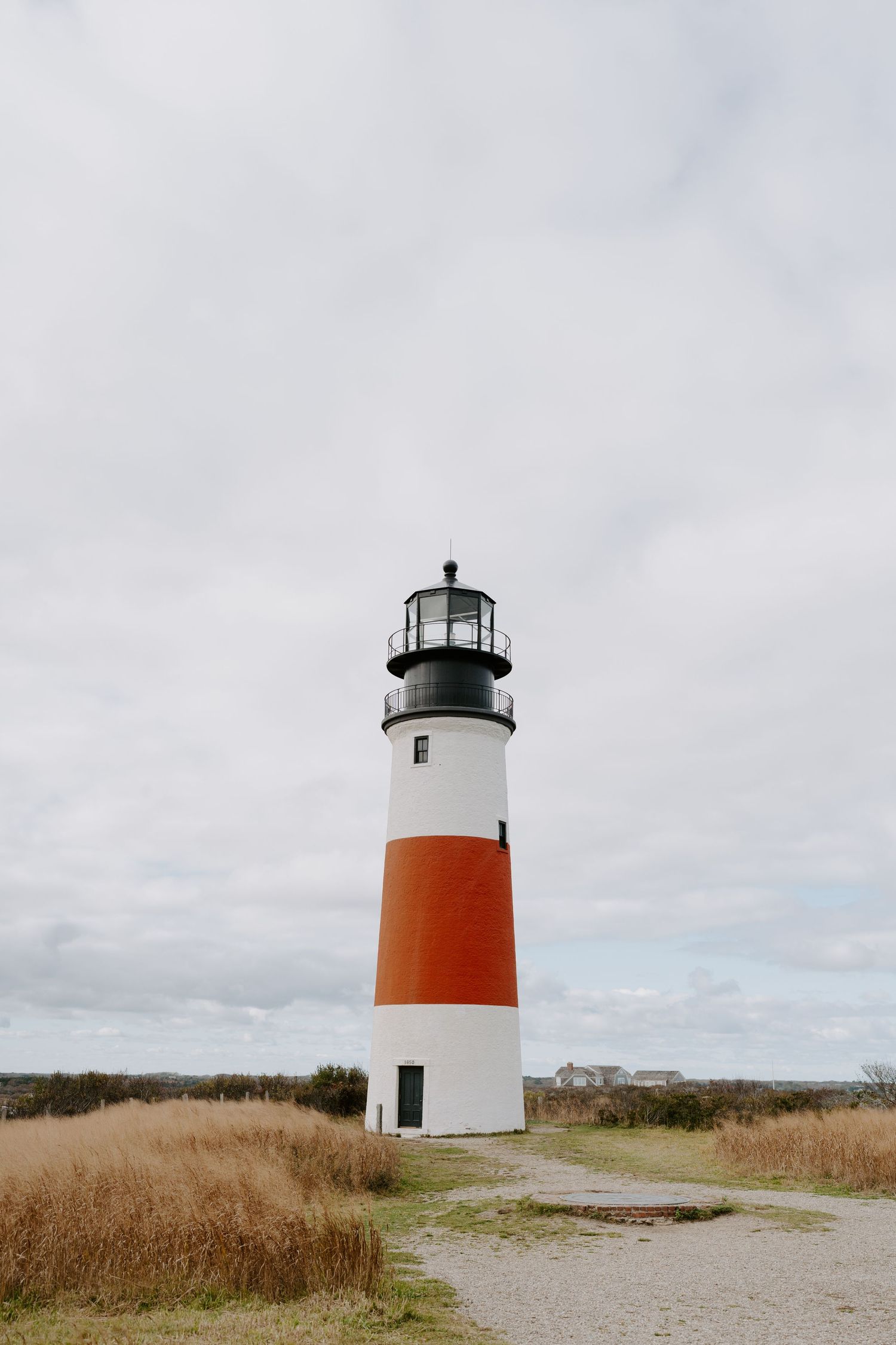 Red and white striped lighthouse stands tall against cloudy sky surrounded by coastal grassland.