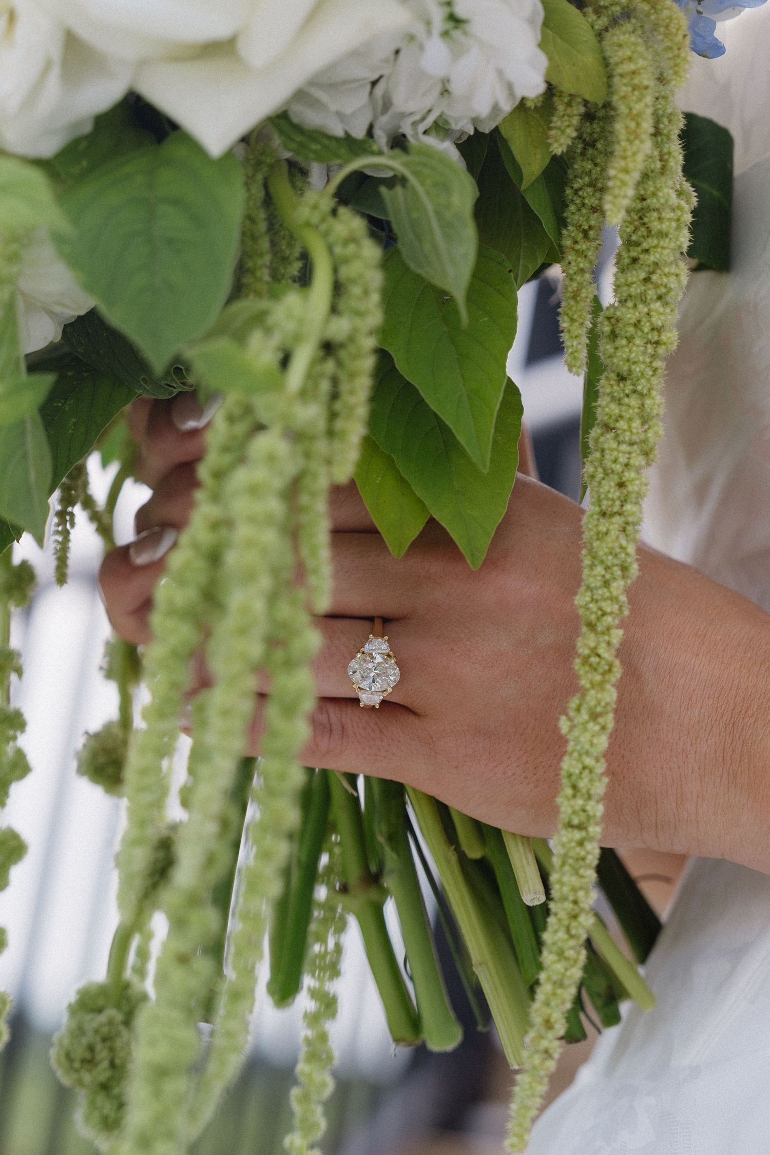 Bride holding a wedding bouquet with green amaranthus, displaying a stunning diamond solitaire engagement ring on her finger.