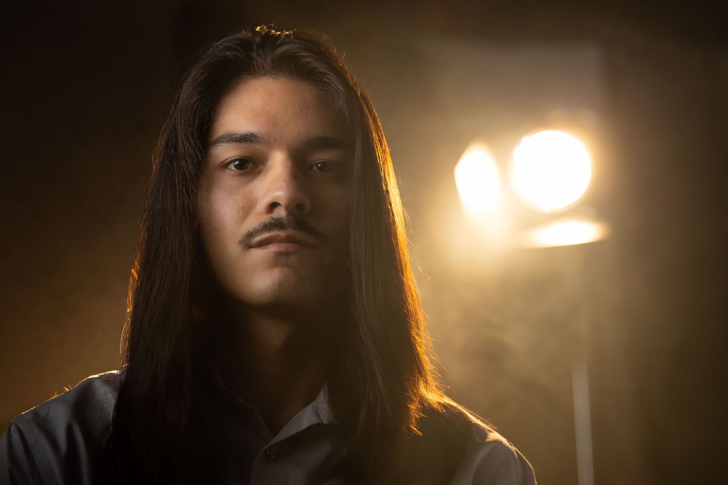 A person with long dark hair in dramatic low-key lighting creates a moody cinematic atmosphere.