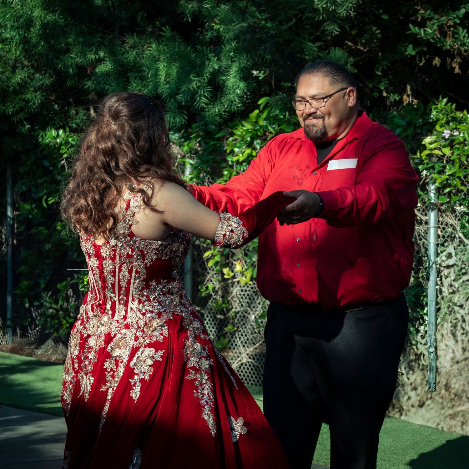 Outdoor photoshoot featuring red formal wear against green foliage.