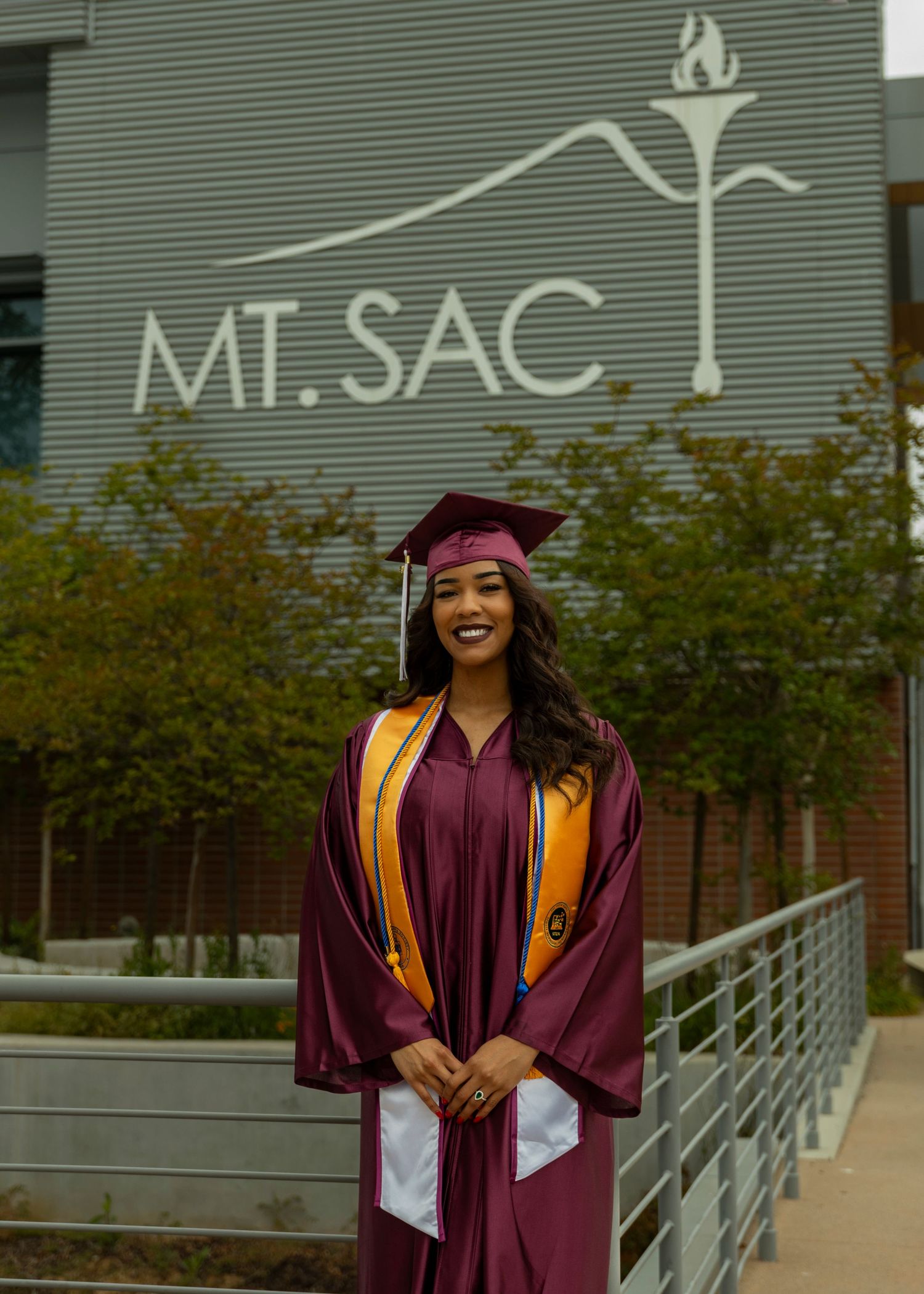 A graduate celebrates with raised arms outside Mt. SAC building on graduation day.