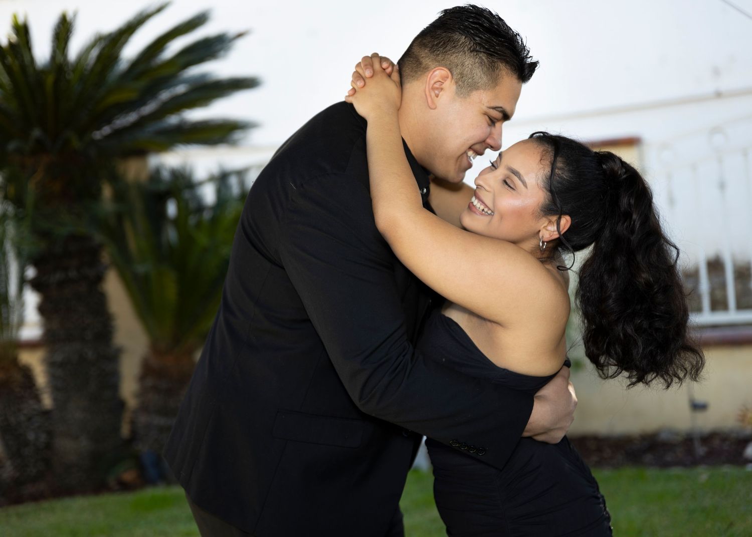 Happy couple in black clothing sharing joyful moment during outdoor photoshoot.