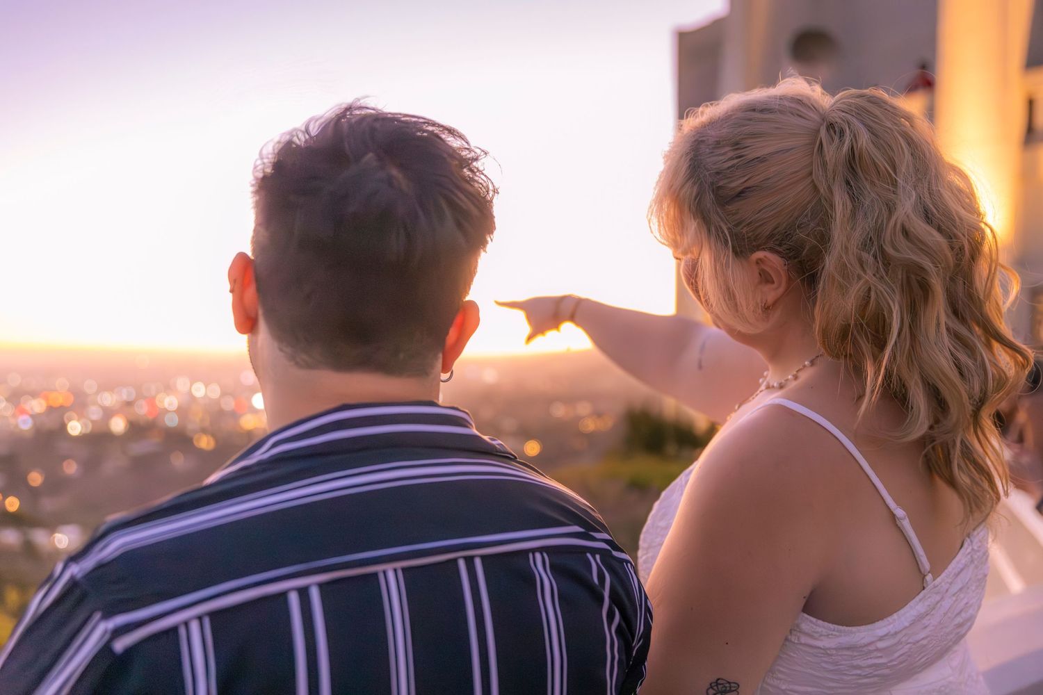 Silhouettes of a couple embrace against a warm sunset sky with mountains visible in the distance.