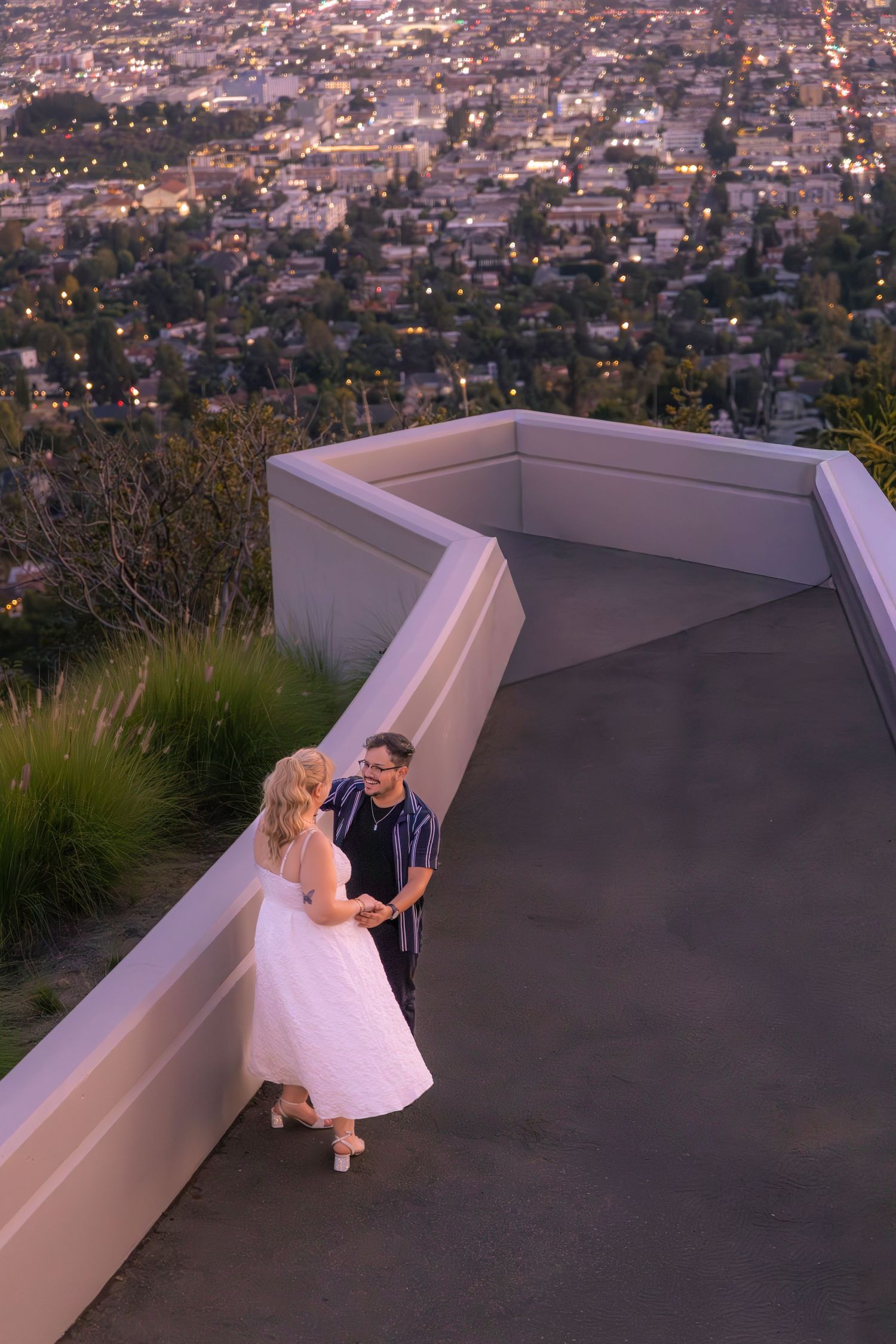 Couple poses on modern rooftop terrace with panoramic city views at dusk.