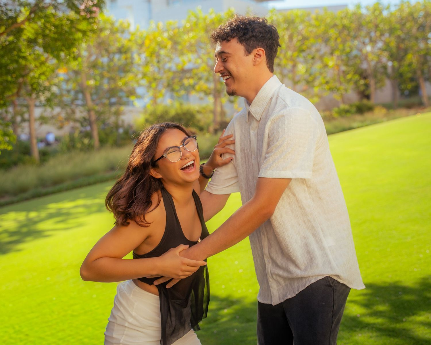 A laughing couple shares a joyful moment together on a bright green lawn outdoors.
