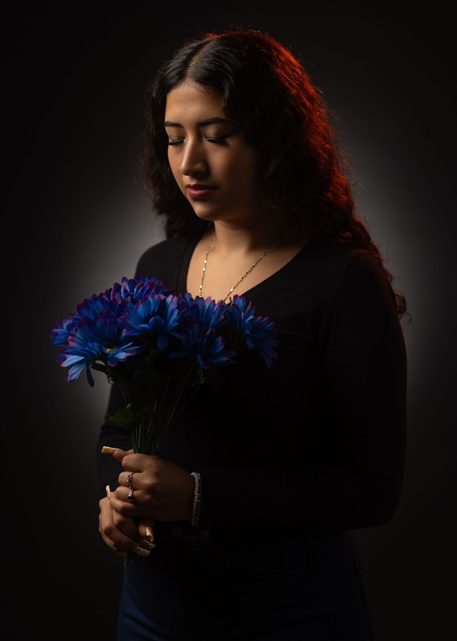 A person in dark lighting holds vibrant blue gerbera daisies in a dramatic artistic portrait series.