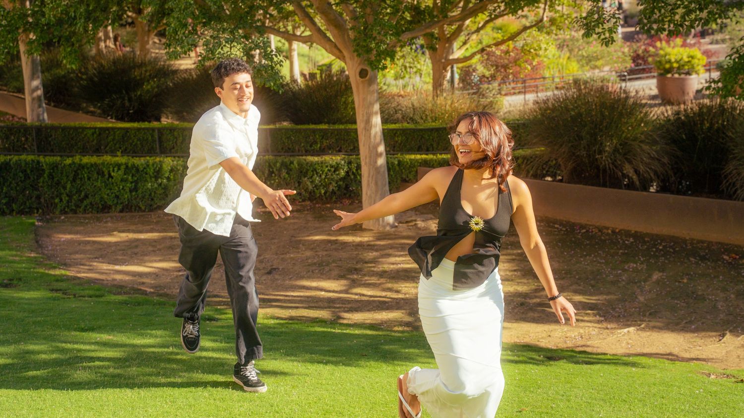 A man and woman dancing outdoors on green grass in a sunny park setting.