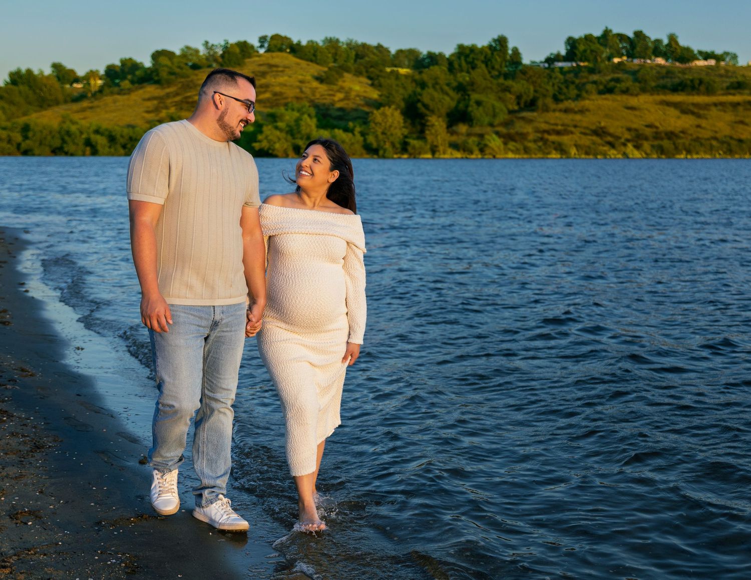 A couple walks along the water's edge at sunset with their feet in the lake.