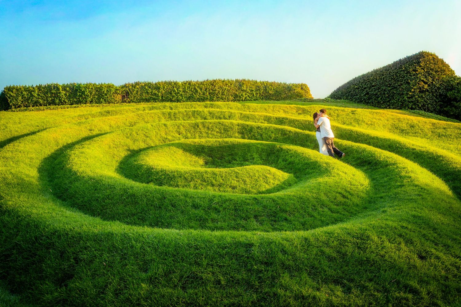 A couple stands together in a beautifully manicured spiral green grass garden landscape.