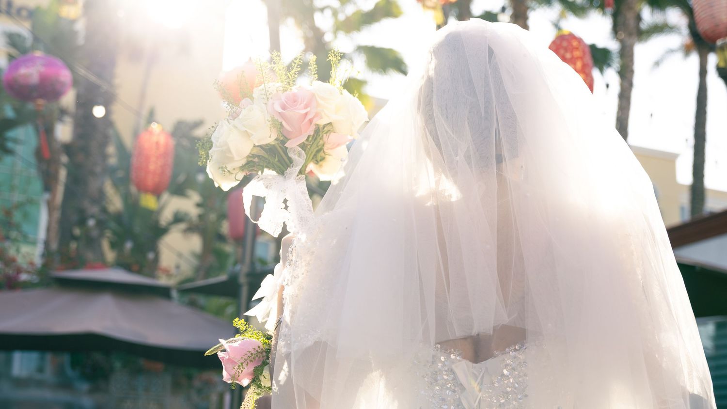 Two white wedding dresses displayed side by side against a sunlit wall with floral decorations.