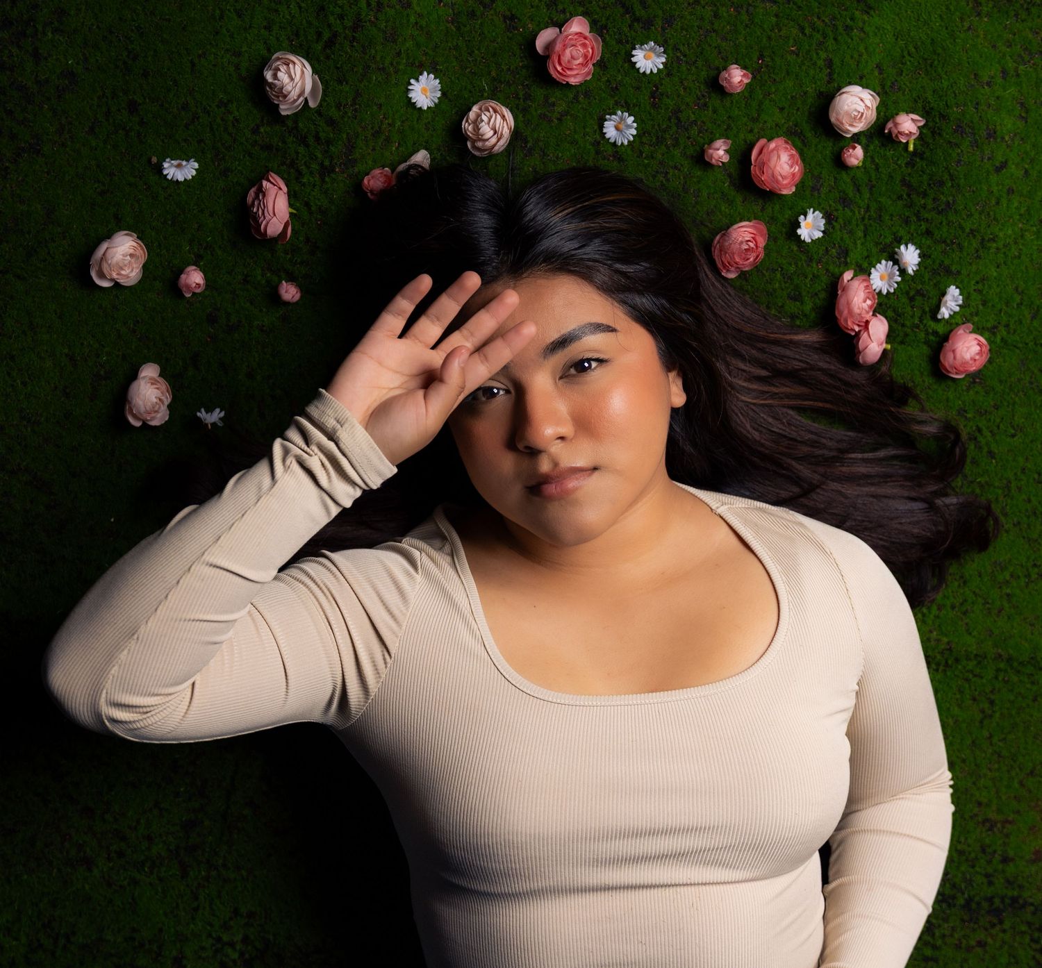 A person in a cream colored sweater poses on green grass with scattered pink flowers.