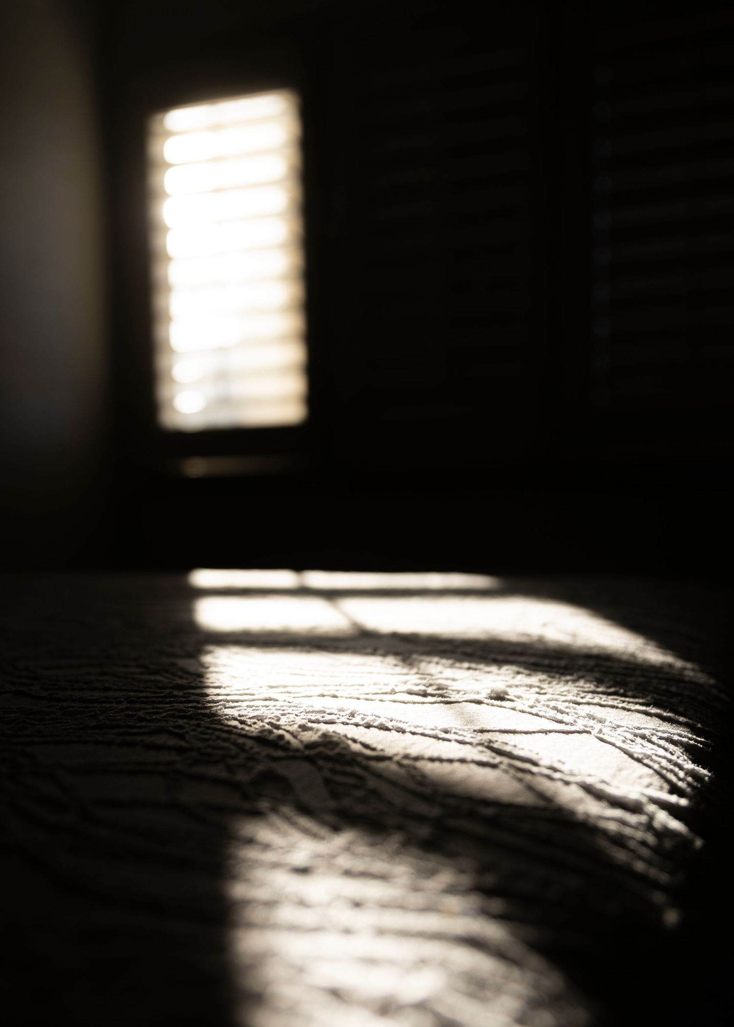 Dramatic shadows and light beams streaming through window blinds onto a textured surface.