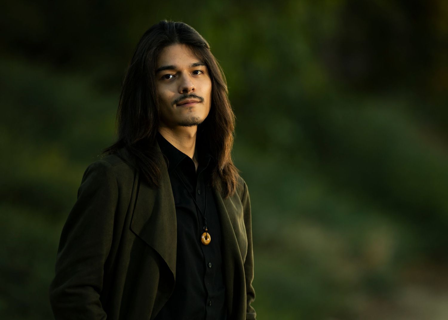 Side profile portrait with long hair against soft focus natural backdrop.