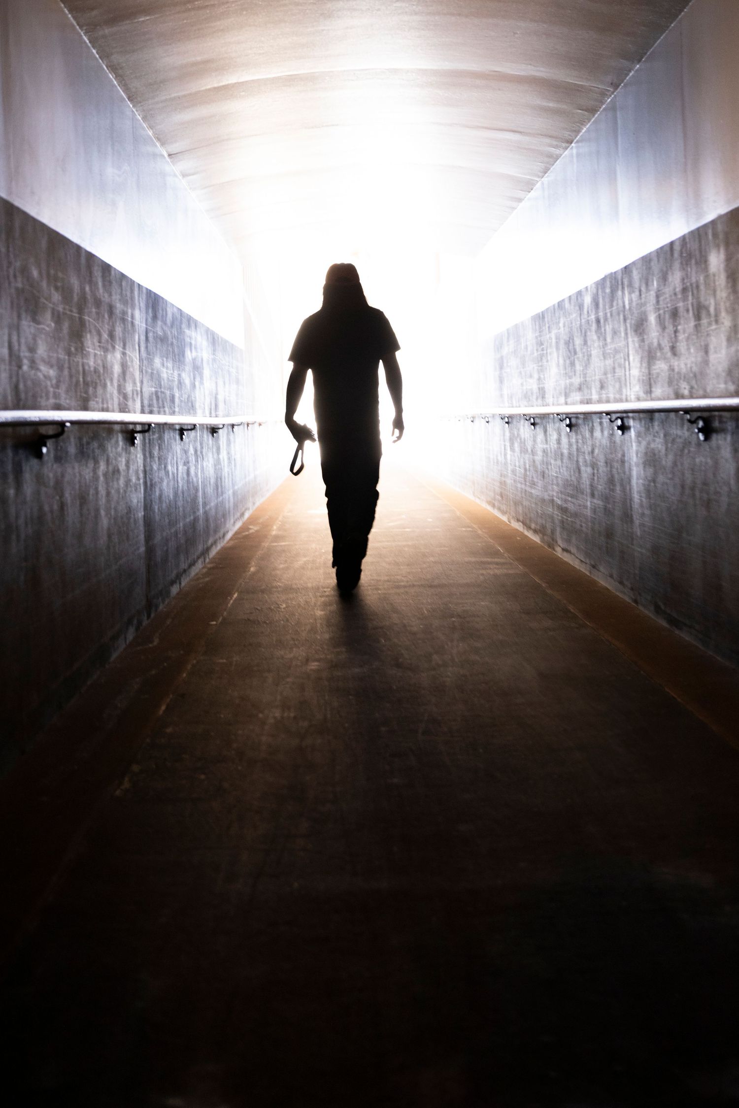 Silhouette walking through a long concrete tunnel towards bright light at the end.