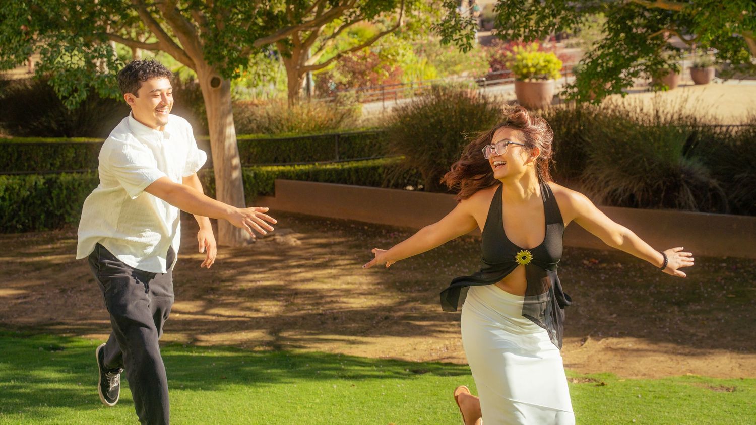 Two people joyfully running toward each other with open arms in a sunny green park setting.