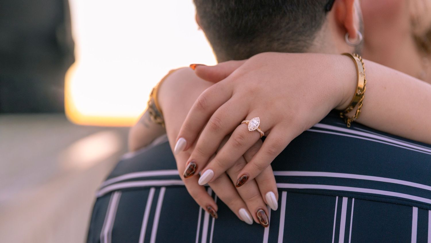 A couple holds hands and embraces during a sunset engagement photo session on a rooftop.