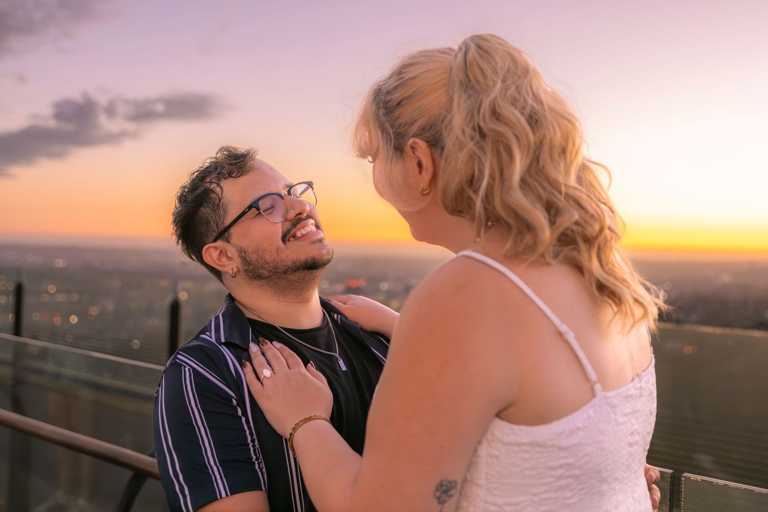 A couple embraces and laughs together on an outdoor deck at sunset with mountains in the background.