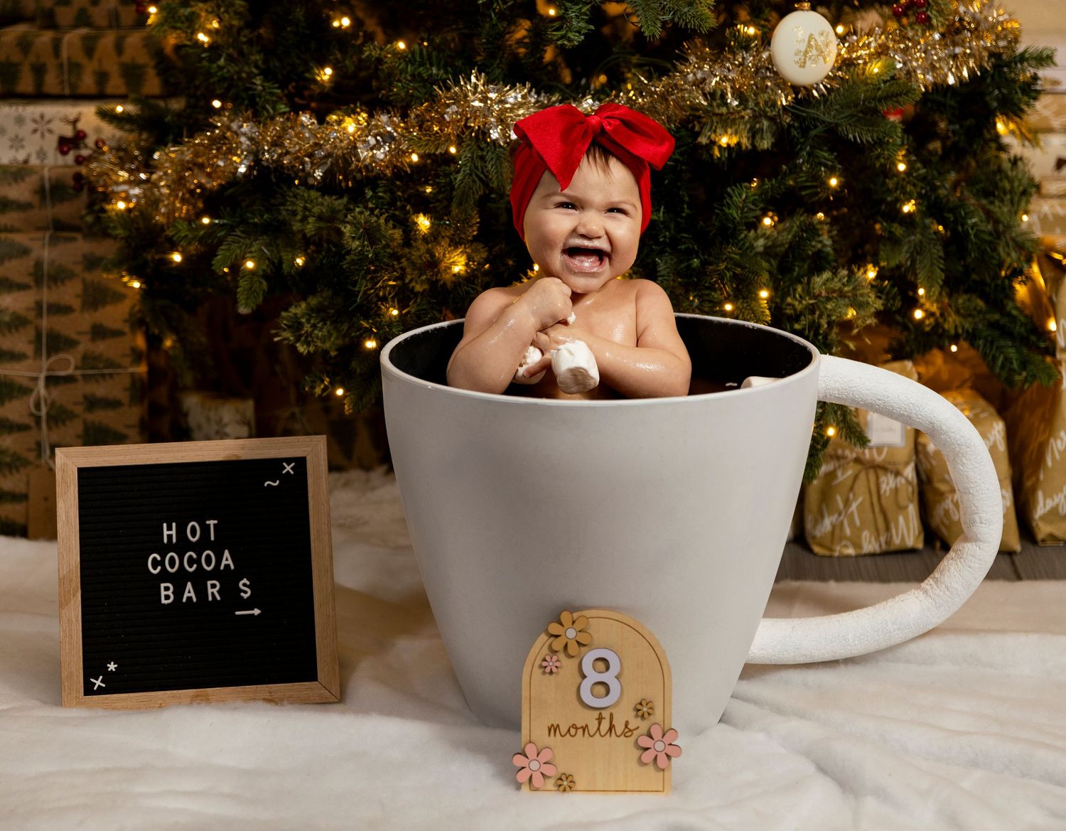 Large decorative coffee cup photo prop with Christmas tree and holiday decorations in background.