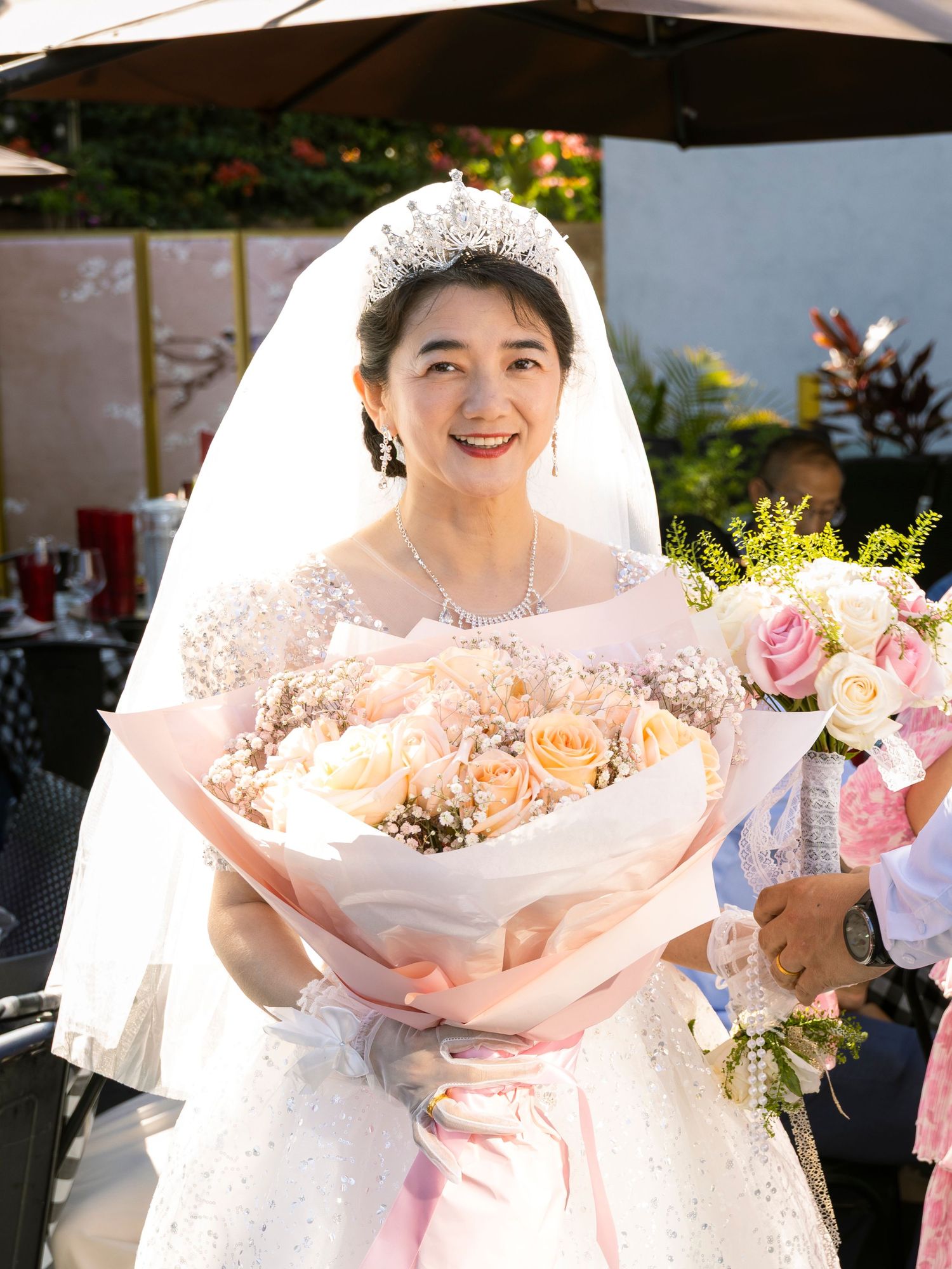 A white wedding dress and bouquet of pink roses are captured in bright natural light.