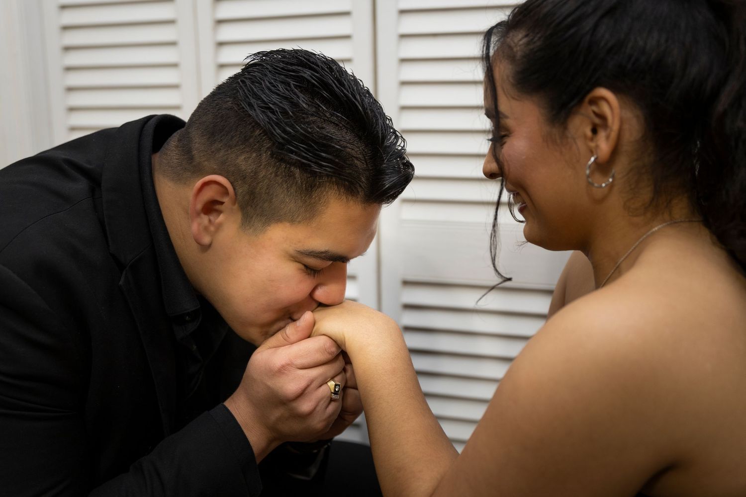 Romantic couple sharing tender moments against white shuttered backdrop.