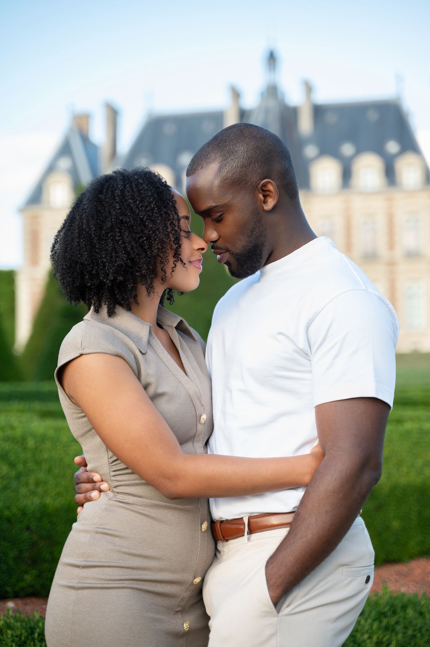 A couple shares an intimate moment in front of a French château, the man in white embracing the woman in a taupe dress.
