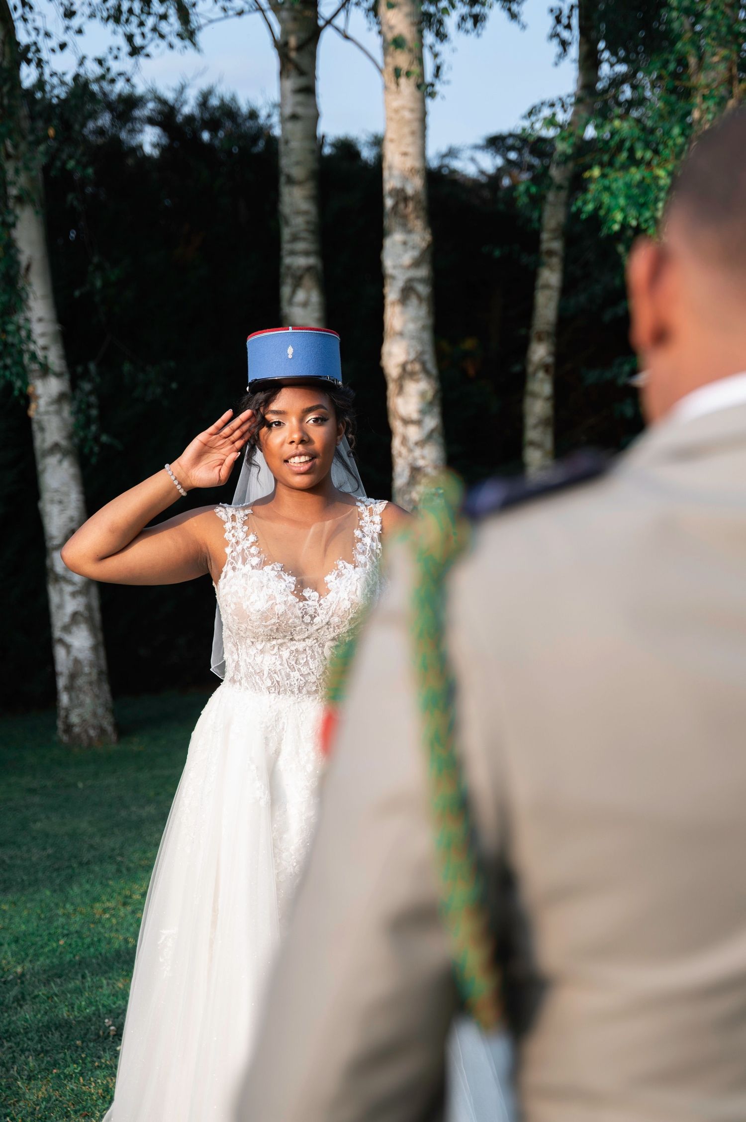 Black bride in lace gown salutes her groom while wearing a blue military kepi hat.